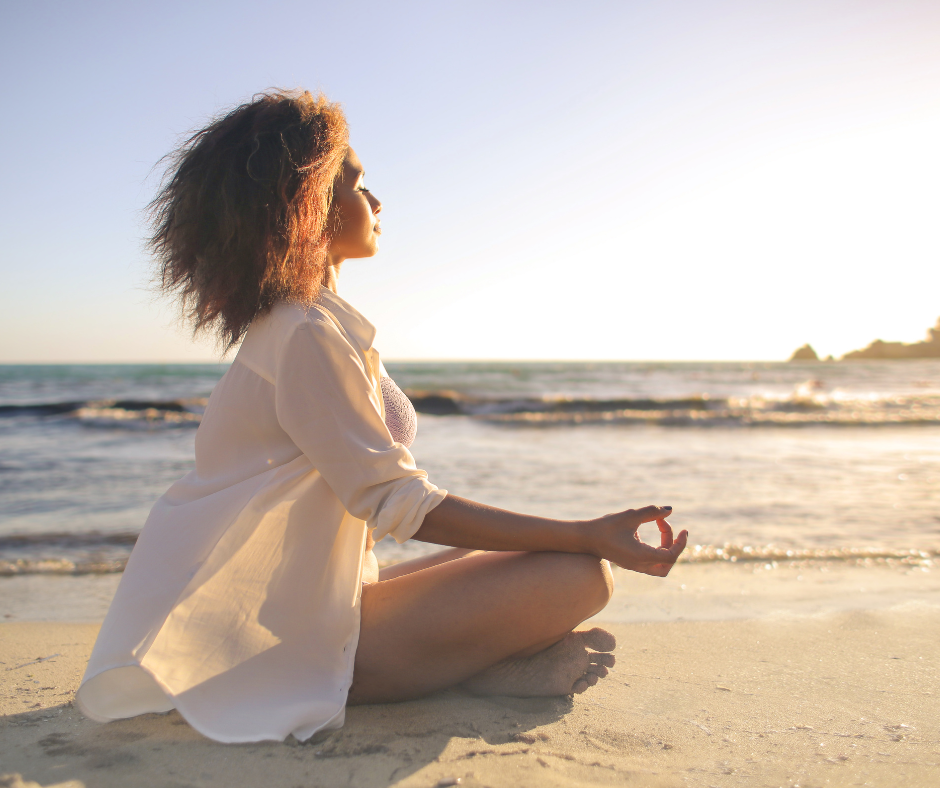 Woman sitting on the beach with the waves in the background in a meditative peaceful pose